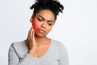 A woman touching her jaw with visible redness, showing discomfort from a toothache or dental emergency.